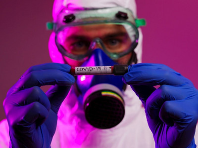 新型冠状病毒感染预防要点摄影照片_冠状病毒，医生拿着阳性新冠病毒血样管。佩戴生物危害流行病防护口罩、防护服、发光。