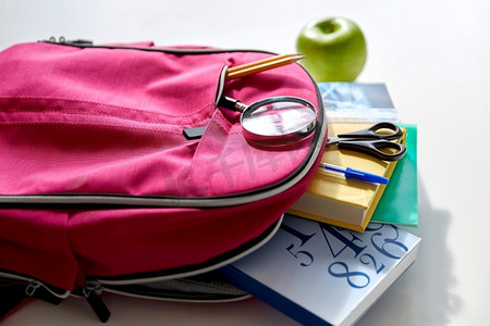 书放在桌子上摄影照片_教育和学习概念—粉红色背包与书籍和学习用品，绿色苹果放在桌子上。背包里装着书本、学习用品和苹果