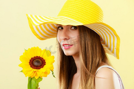 黄色背景下手持向日葵、头戴草帽的夏日美女特写
