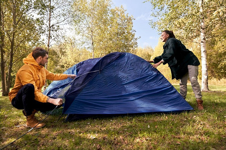 秋天野营摄影照片_露营、旅游和旅行概念-幸福的情侣在户外搭帐篷。幸福的一对夫妇在户外搭帐篷