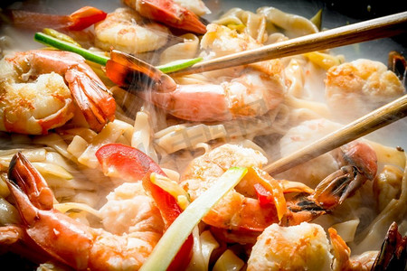 热热的面条摄影照片_热腾腾的中国炒面，配上酱汁、虾和蔬菜。在乡村背景下。热腾腾的中国炒面，配上酱汁、虾和蔬菜。