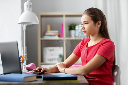 儿童，教育和学习概念—十几岁的女学生在家里与笔记本电脑。学生女孩与膝上型计算机学习在家里