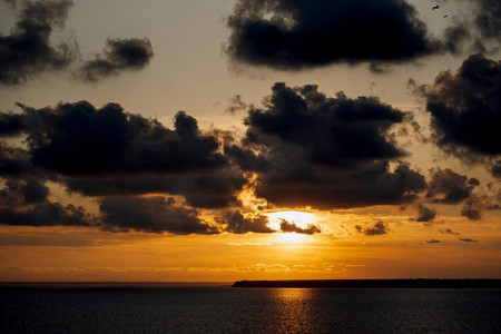 橙色的夕阳落在海面上，天空中有云