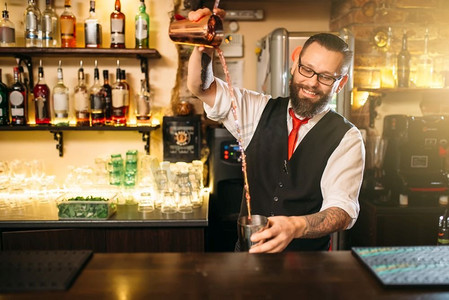混合酒精饮料摄影照片_酒吧柜台后面的酒吧服务员表演。帅气的酒精饮料制备