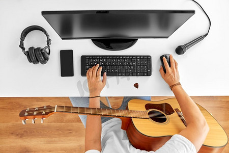 休闲，音乐和人的概念—年轻人或音乐家与电脑和吉他坐在桌子。年轻人与电脑和吉他在桌子上