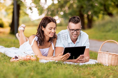 与人连接摄影照片_休闲与人概念—快乐夫妇与平板电脑电脑在夏季公园野餐。愉快的夫妇与平板电脑在野餐在公园