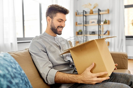 邮件递送，发货和人的概念—快乐的微笑男子打开包裹箱在家里。快乐的微笑男子打开包裹盒在家里