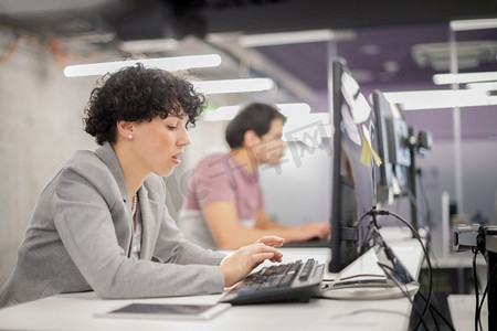 年轻的女性软件开发者使用桌面计算机，同时写编程代码在现代创意创业办公室