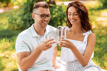 休闲与人概念—快乐夫妇在夏季公园野餐饮料。快乐的夫妇干杯饮料在夏季公园