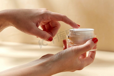 美容产品、化妆品和人概念—女性手拿着罐保湿霜在米色背景一种女性手持保湿霜罐
