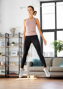 健身跳摄影照片_运动、健身和健康的生活方式概念—年轻妇女在家里锻炼和跳跃。年轻女子在家里锻炼