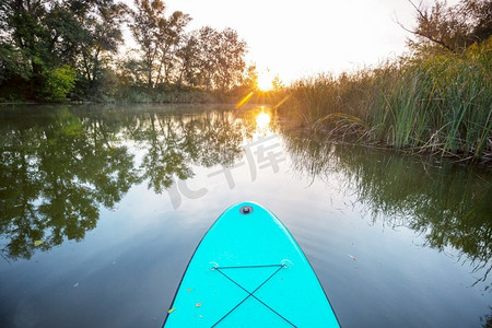 sup充气桨板摄影照片_日出时夏天河上的充气划桨板