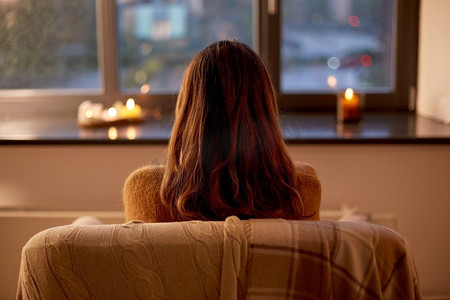 正在燃烧的蜡烛摄影照片_万圣节，卫生，休闲的概念-秋天的女人在家中透过窗户看。秋天在家中透过窗户看着的女人