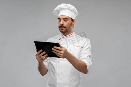 烹饪、烹饪和人的概念-身穿连衣裙的男厨师，在灰色背景下使用平板电脑。配备平板电脑的男厨师
