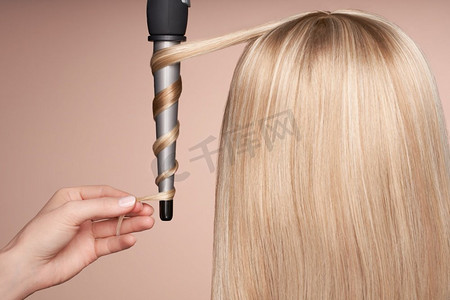 卷发的摄影照片_理发师用卷发棒把长发卷起来。美丽的女人与长的直头发。光滑发型