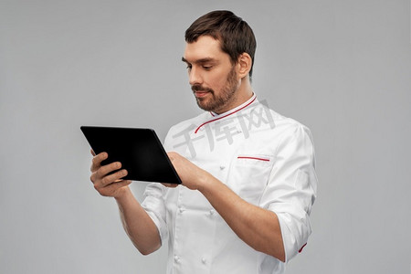 烹饪，烹饪和人的概念-男厨师，在灰色背景下使用平板电脑。配备平板电脑的男厨师