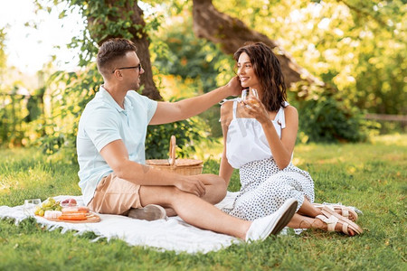 休闲和人的概念快乐的夫妇与饮料和食物在夏季公园野餐。一对幸福的情侣在夏季公园野餐