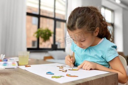 云层上摄影照片_童年、爱好和休闲的概念--小女孩在家里用毛笔画木质硬纸板物品。小女孩在家里画木制品