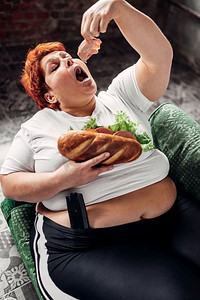 肥胖女性摄影照片_超重女人吃三明治，暴食症，肥胖问题。不健康的生活方式，肥胖的女性。超重的女人吃三明治，暴食症，肥胖