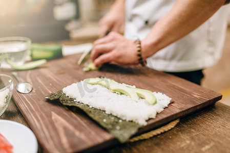 海鲜制作摄影照片_男厨师的手，做寿司卷，海鲜。传统的日本料理，准备过程。男厨师亲手制作寿司卷、海鲜