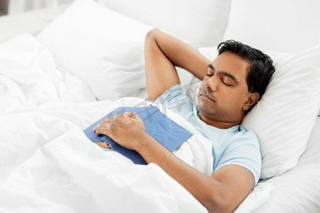 人，睡觉时间和休息的概念--印度男人在家睡觉时看书。一名印度男子拿着书睡在家里的床上
