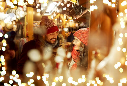 寒假和人们概念快乐的年轻人在圣诞集市的傍晚灯火通明。圣诞集市上的快乐情侣在彩灯下