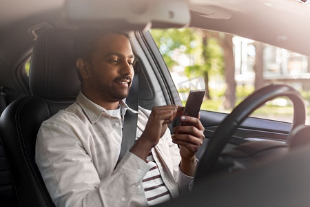 交通、人和科技概念-微笑的印度男人或司机在车内使用智能手机。微笑的印度男子在车里使用智能手机