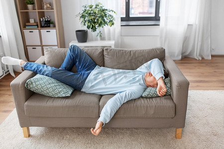 懒人投资摄影照片_人，无聊和抑郁的概念—无聊或懒惰的年轻人躺在沙发上在家里。无聊或懒惰的年轻人躺在家里的沙发上
