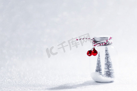 玻璃罐的圣诞装饰品与条纹丝带，铃铛和冷杉树在雪里面在闪光背景。玻璃罐圣诞饰品