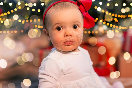 圣诞节圣诞树彩灯摄影照片_节日和童年的概念-圣诞树上的美丽女婴。圣诞树彩灯下的美丽女婴