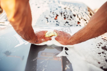 男性用手摩擦汽车上的泡沫，汽车上的肥皂水。洗车站。男性用泡沫擦车，洗车