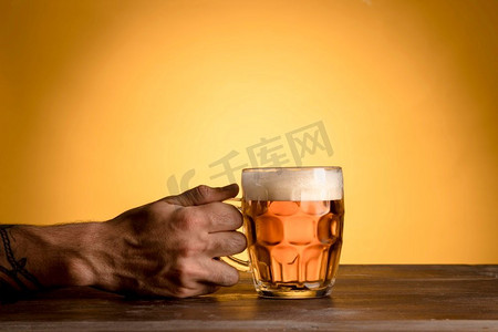拿着照片摄影照片_男人拿着玻璃啤酒木桌。高分辨率照片。男人拿着玻璃啤酒木桌。高品质的照片