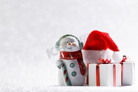 雪人摄影照片_圣诞雪人带着礼物和圣诞老人帽，背景鲜艳。带着礼物的圣诞雪人