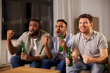 喝啤酒摄影照片_友谊、情感和休闲概念—快乐微笑的男性朋友或球迷在家里喝啤酒。快乐的男性朋友或球迷在家里喝啤酒