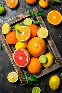 柑橘摄影照片_成熟的柑橘类水果与叶子在托盘。在黑色的乡村背景。成熟的柑橘类水果与叶子在托盘。