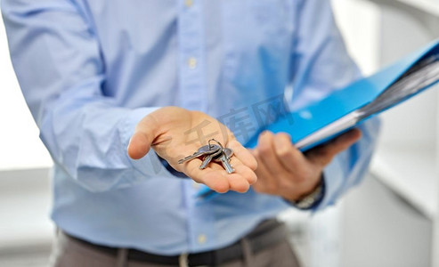 房地产，住房和人的概念-男人手握房屋钥匙和文件夹的特写。男性手持钥匙和文件夹的特写镜头