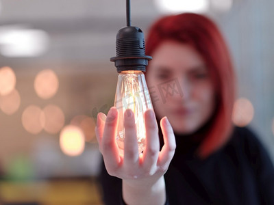 红头发女商人在办公室拿着一只手围绕代表企业解决方案概念和绿色能源的灯泡