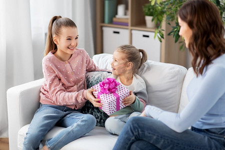 人，家庭和假期概念—两个女儿在家里给快乐的母亲送礼物。女儿给快乐的母亲送礼物