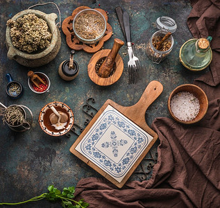 各种质朴的陈旧厨房用具，在深色的桌子背景上，有砧板、叉子和干调味品。顶视图
