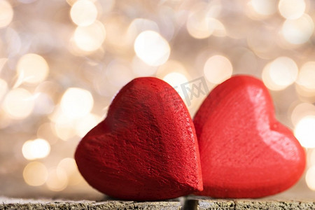 两个小手工制作的红木心在明亮的金色光bokeh背景情人节卡。两颗心在散景背景