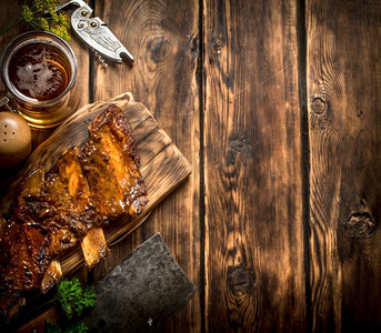 烧烤啤酒摄影照片_与肉斧和啤酒一起烤的排骨。在一张木桌上..与肉斧和啤酒一起烤的排骨。