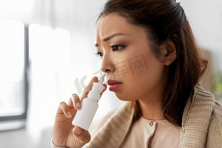 喷口水摄影照片_健康、寒冷和人的概念-悲伤生病的年轻亚洲妇女在家里用毛毯喷鼻。生病的亚裔妇女在家中服用鼻腔喷雾剂