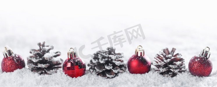 冬季圣诞装饰的红色圣诞装饰球排成一排，雪地上的松果隔绝在白色背景上。冬季圣诞装饰