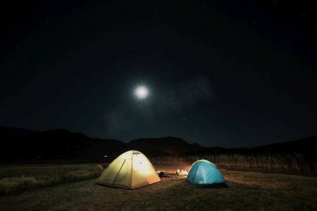 在月亮下的山上露营。一个搭起的帐篷在天空下闪闪发光。夜山草甸间露营的旅游帐篷