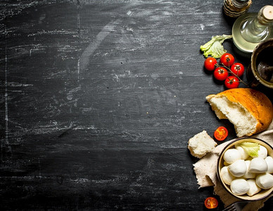 奶酪背景摄影照片_马苏里拉奶酪配新鲜面包、西红柿和蔬菜。在黑色的木质背景上..马苏里拉奶酪配新鲜面包、西红柿和蔬菜。