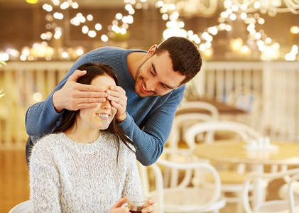 节日灯光摄影照片_人们，惊喜和约会概念—快乐的夫妇喝茶咖啡馆或餐馆在节日灯光。快乐的夫妇喝茶在咖啡馆