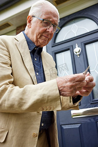 钥匙男人摄影照片_困惑的老年人与早期痴呆症试图找到正确的门钥匙在房子外面
