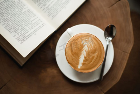 一杯咖啡摄影照片_打开书本，一杯咖啡放在木桌上。