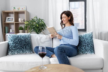 女人坐着摄影照片_人与休闲的概念--快乐的年轻女子坐在沙发上，在家看书。一位年轻女子在家看书