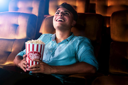 在剧院电影院看电影时，一个年轻人微笑着吃着爆米花